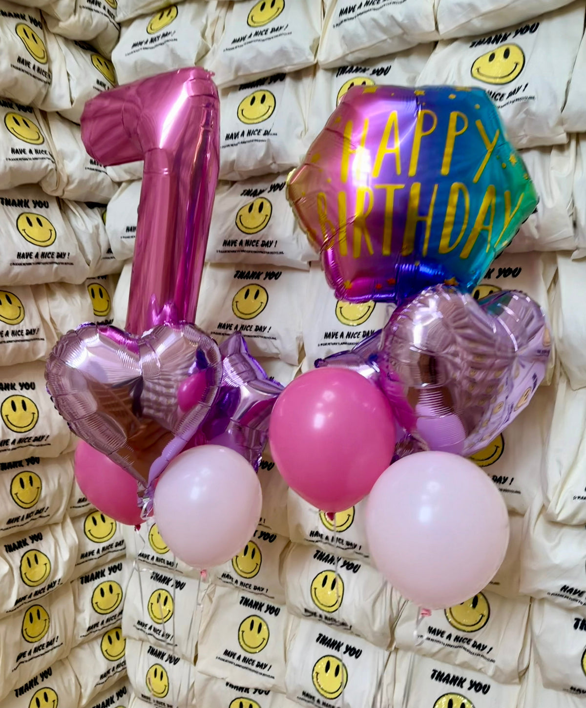 Two first-birthday helium balloon bouquets with a pink number 1, a rainbow Happy Birthday balloon, pink foil hearts and pink latex balloons